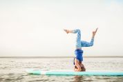 Frau macht Kopfstandübung auf einen Surfbrett auf dem Wasser yoga-auf-dem-surfbrett